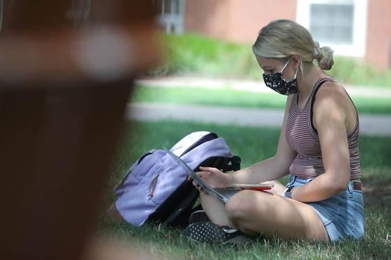 Photo of a masked female Chatham University student working on her laptop outside on Shadyside Campus